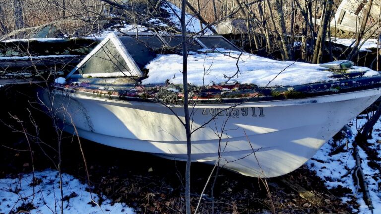 An abandoned boat rests beneath the remains of a fallen garage in Borups Corners. Once a vessel of open water, it now holds the stillness of forgotten years.