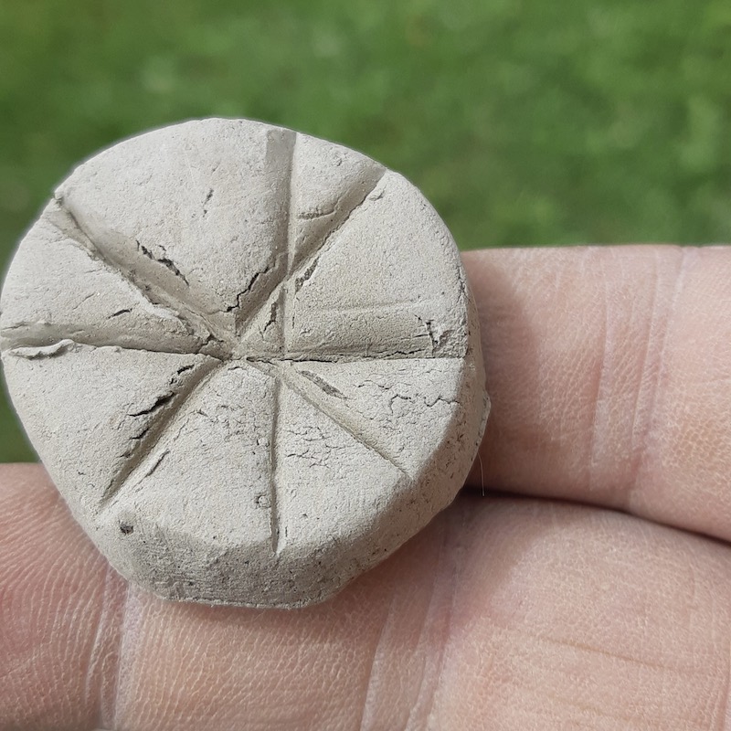 The same puck after a few hours of drying in the sun. The small, rough tears inside the pressed lines have stayed the exact same size, showing the clay didn't split open or pull apart as the water evaporated.