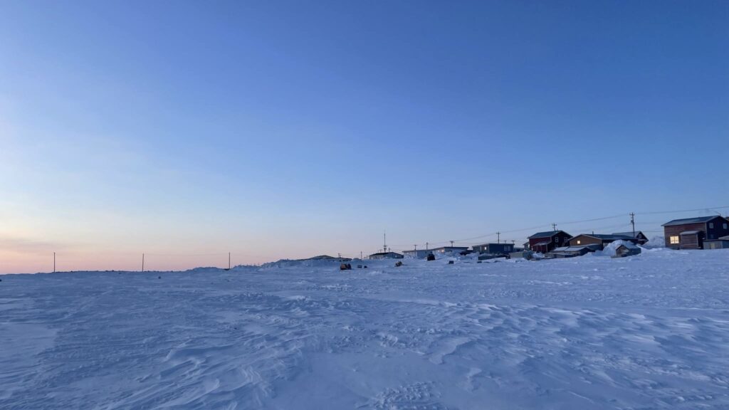 Sky and snow, meeting our homes. A soft light touches everything. Familiar shapes, but a different feel in the air. The edge of our community, where the wild meets our lives. We watch, we remember, we see the subtle shifts in the world around our doors. This is our place, changing with the light.