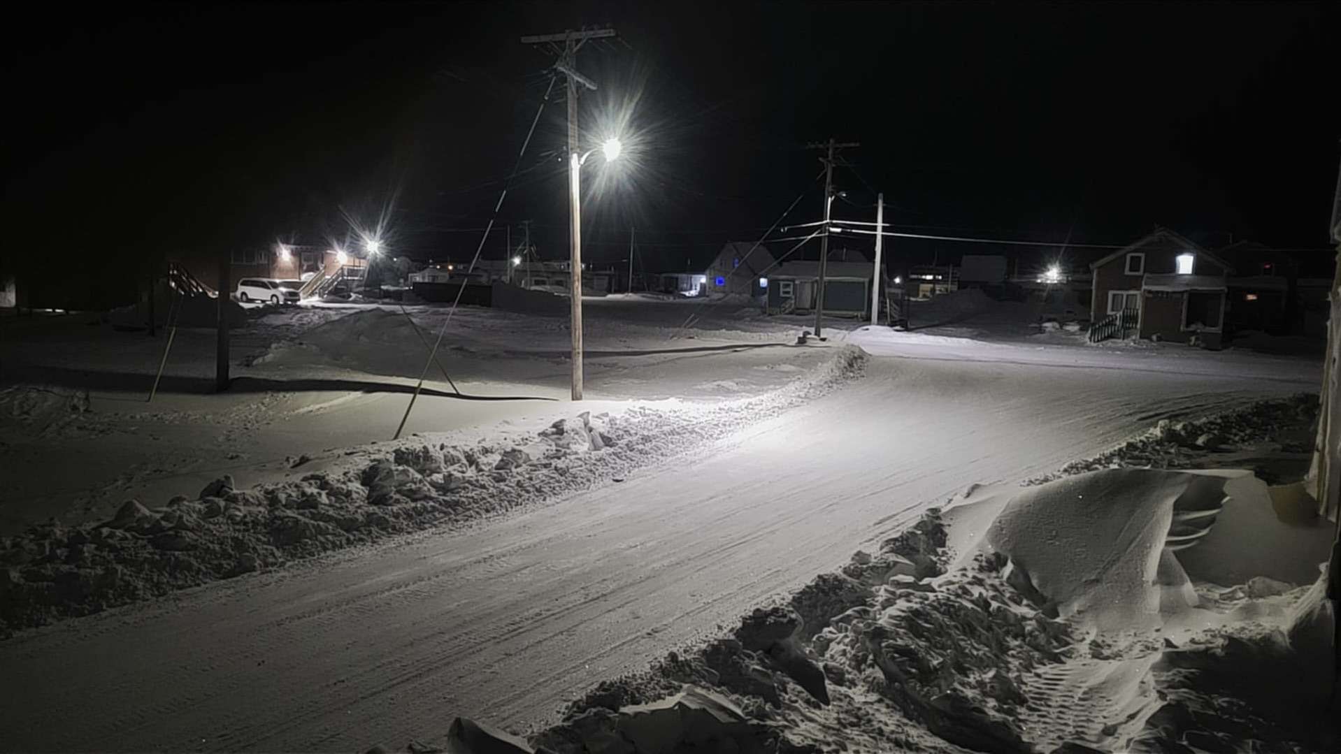 In the quiet Arctic night of Arviat, streetlights cast a soft glow against snowbanks, their light fading into the vast, dark sky. The stillness of the landscape is broken only by the crisp, cold air, as the night embraces the town in its quiet solitude.