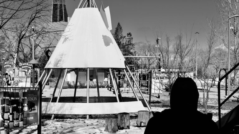 In Winnipeg’s playgrounds, metal tipis rise like echoes of old songs, catching sky in their spines. These are not structures but spells—frames for imagined fires and stories unspoken. Here, laughter roots in the dust, spiraling upward. Memory plays barefoot, circling the sacred geometry where past and future quietly braid. Photo: Jamie Bell