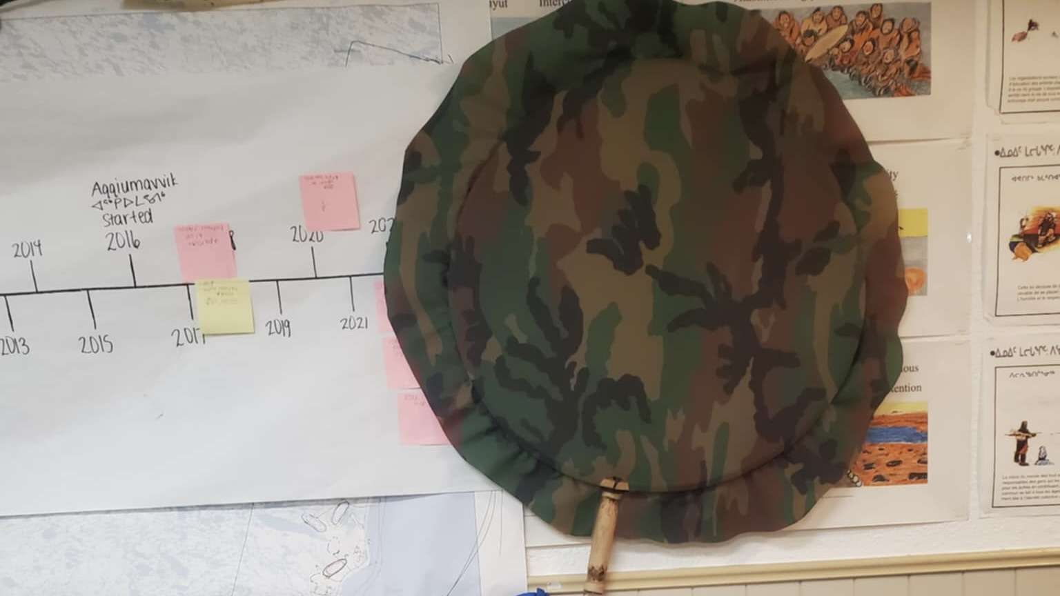 A qilaut (ᖃᓕᐊᐅᑦ) hangs quietly on the wall, camo-covered and well-worn, waiting to be lifted—its silence holding generations of rhythm, memory, and story. Photo: Eva Suluk