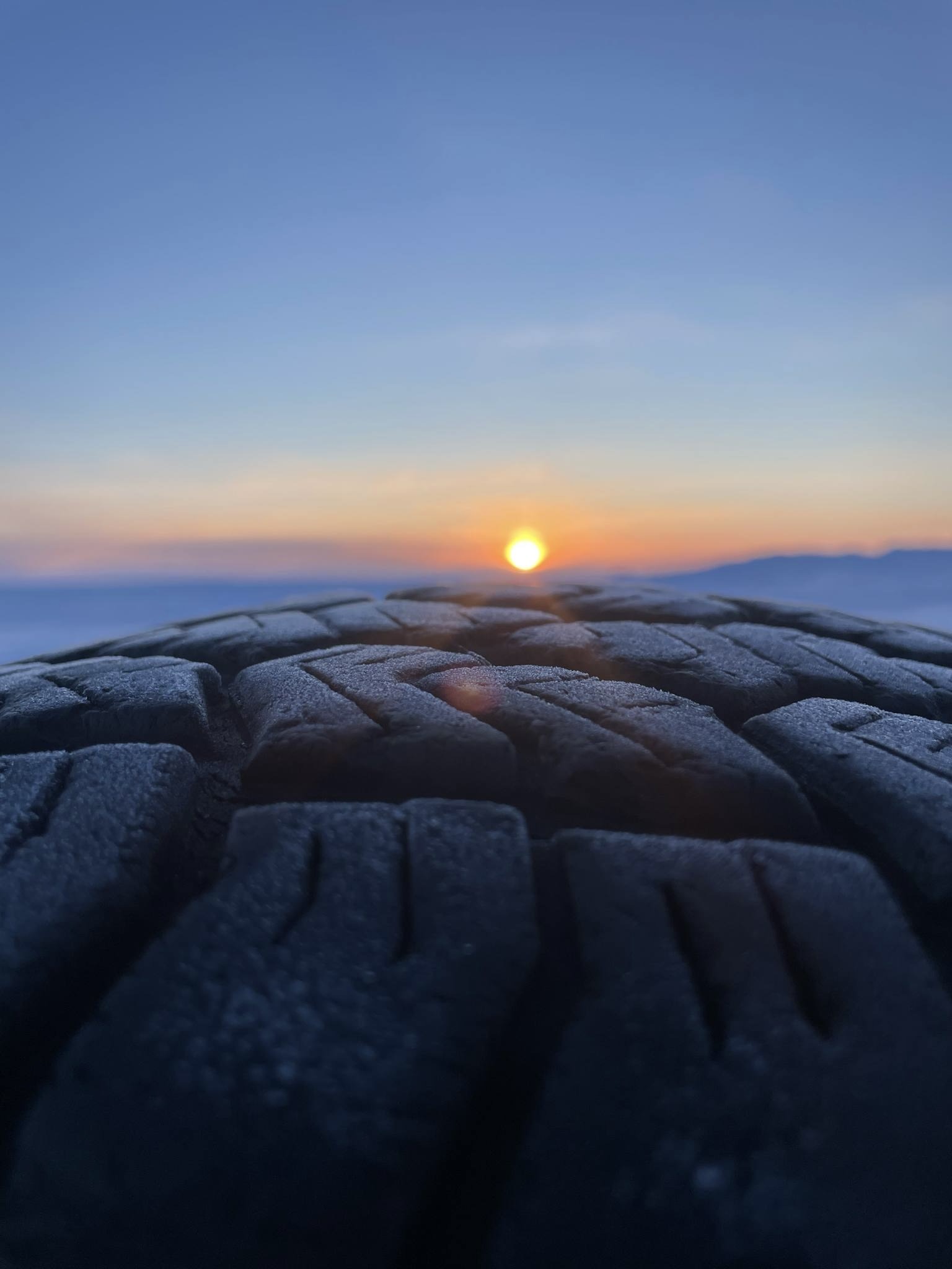 Rubber and frost meet, right here. Where have we been? Where are we going? That horizon... it's softer now, the light uncertain. Each mark on this tire, a story of the land. But the land is changing, breathing differently. I see it, we all do. This isn't just a view; it's the ground shifting beneath us, captured in a moment.