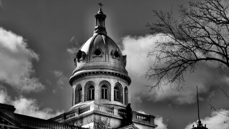The dome of the St. Boniface Archdiocese rises with quiet dignity over Winnipeg’s historic French quarter, a structure as solemn as it is beautiful. Caught in the crisp contrast of winter sun and shadow, the building’s architectural grace tells a story of leadership and legacy. The Romanesque lines and tall, narrow windows evoke the traditions of the Church, while its presence reminds visitors of the enduring role St. Boniface has played in shaping Métis, Francophone, and Catholic identities.
