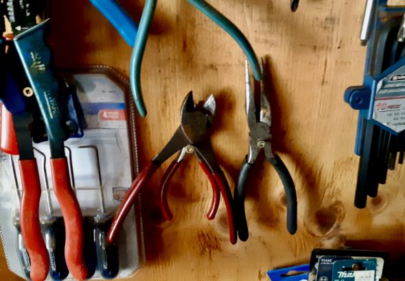 Side cutters and pliers hang ready on the plywood wall of the workshop.