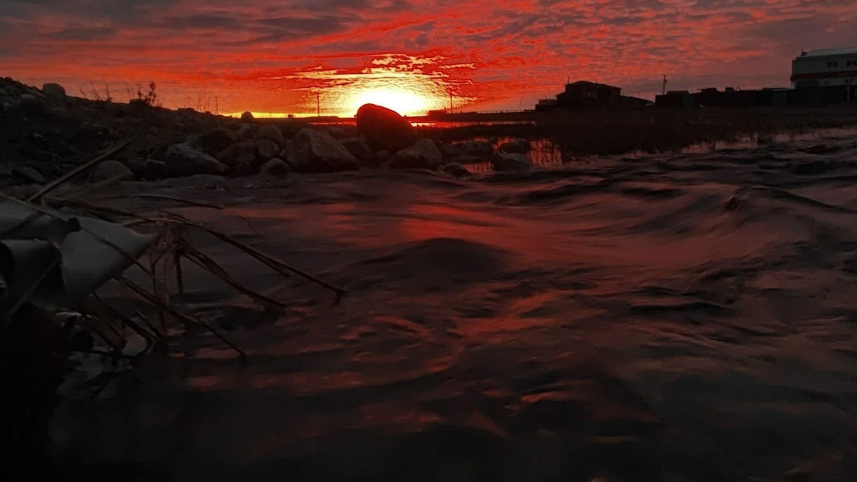 Silhouettes, rocky shores, and crimson waves. Just a tiny human standing on the edge of a giant, glowing world.