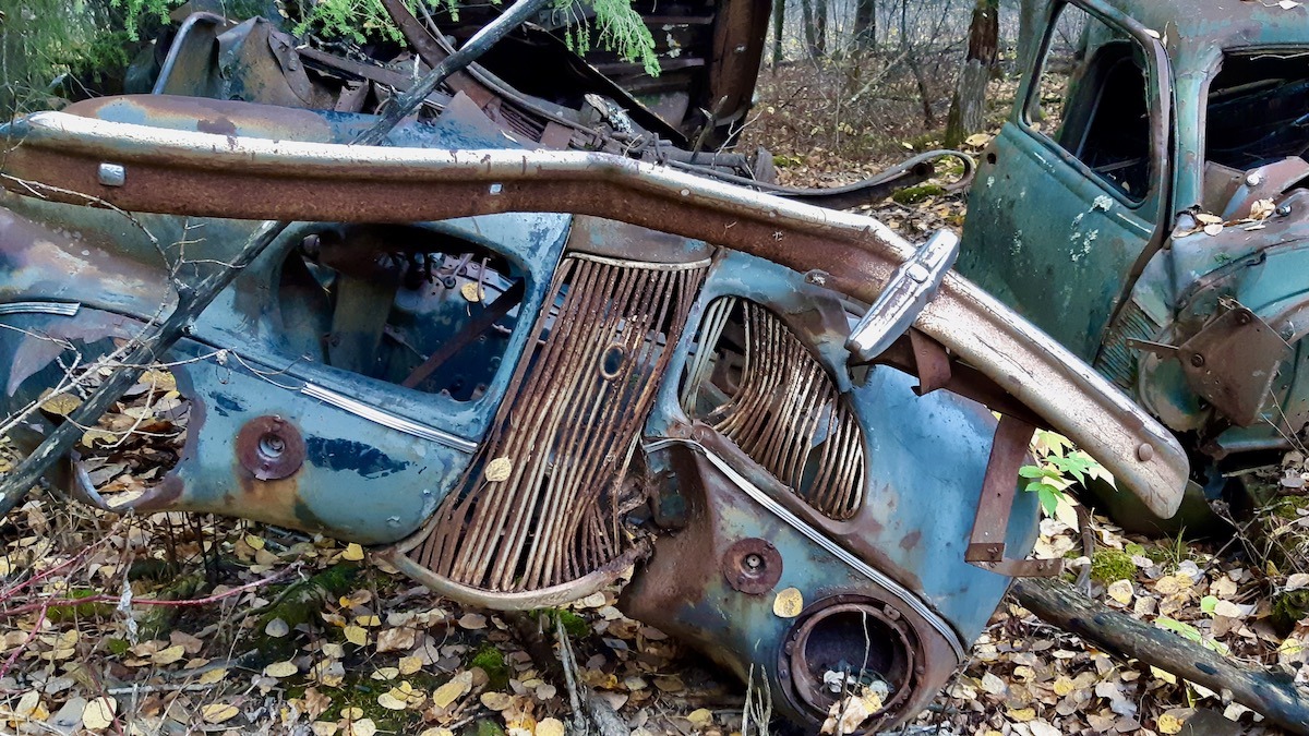 Heavy chrome, dense vertical grille ribs, and teardrop headlight pods reveal the unmistakable front end of a 1938 Dodge Series D8 resting quietly in the underbrush.
