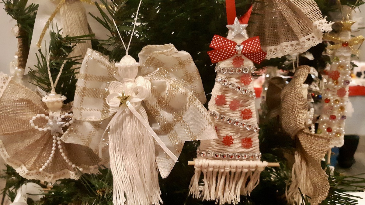 A vibrant display of festive creations includes patterned bow angels and yarn-wrapped Christmas trees adorned with rhinestones, sequins, and red ribbon. Each detailed ornament reflects the artist's dedication to creating memorable, high-quality holiday keepsakes.